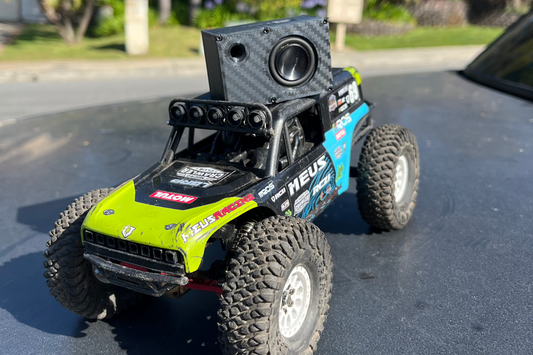 The Mini mounted upright on the roll cage of a green and blue comp crawler on tarmac. 1/24 and 1/18 scale.