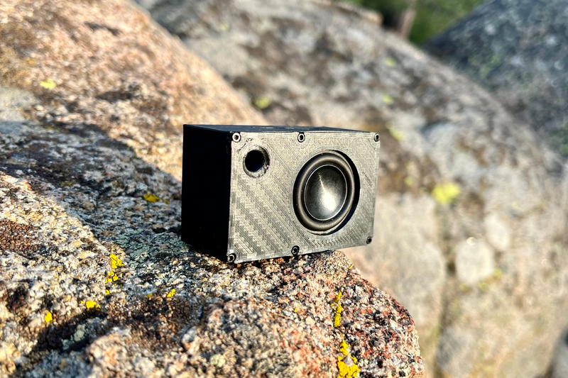 The Mini angled on granite, one 1-inch driver beside a round port in a carbon-look shell. 1/24 and 1/18 scale RC speaker.