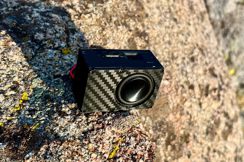 The Single seen from the side, carbon-look weave running across the box, wedged on a granite slab. 1/24 and 1/18 scale.