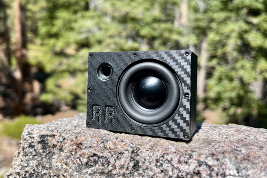 The Super Single square to the camera on granite, carbon-look face with black driver and port. 1/10 scale RC speaker.