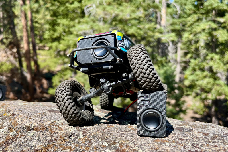 A blue and green comp crawler climbing granite with The Single mounted across the top of its roll cage. 1/24 and 1/18 scale.