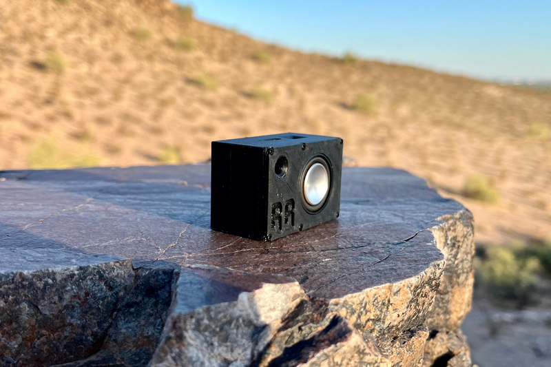 The Mini alone on a dark rock slab with dry desert hills behind. 1/24 and 1/18 scale RC speaker.