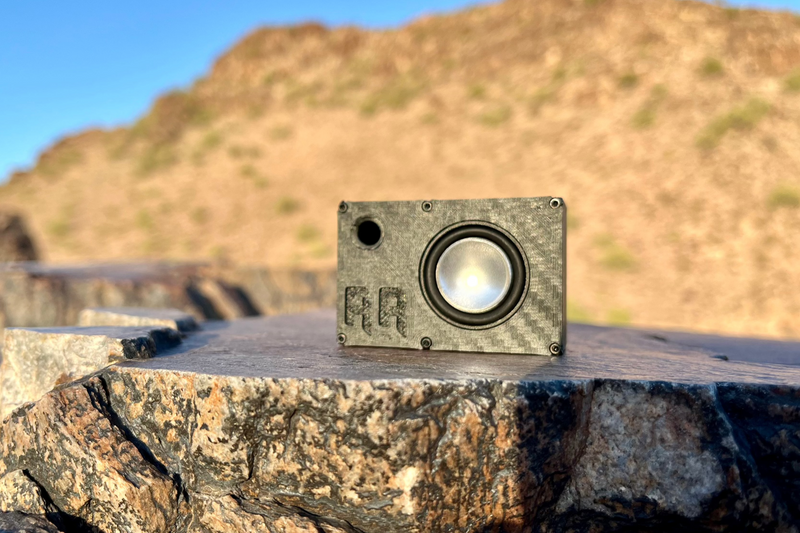 The Mini face on with the embossed RR logo, standing on flat desert rock. 1/24 and 1/18 scale RC speaker.
