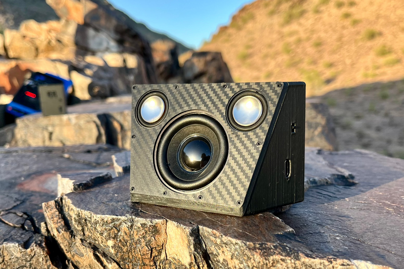 The Overkill for Hardline Bed on desert rock, a wedge-shaped enclosure with one large yellow-cone driver and two smaller drivers. 1/10 scale RC speaker.