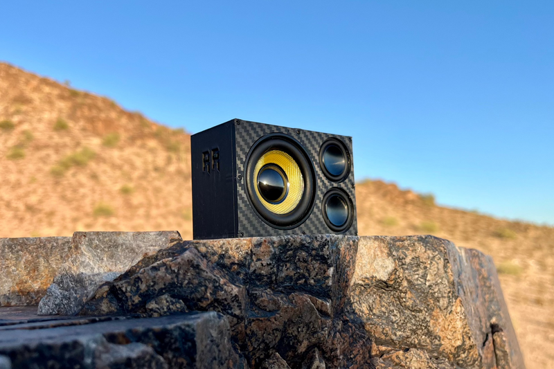 The Overkill perched on dark rock against blue sky with all three drivers visible. 1/10 scale RC speaker.