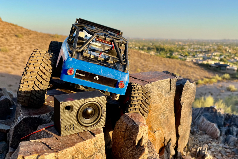 The Supreme Single on a rock ledge below a blue RC crawler, city and hills in the distance. 1/10 scale.