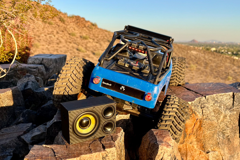 The Overkill sitting on a rock while a blue RC crawler works over the ledge above it. 1/10 scale.