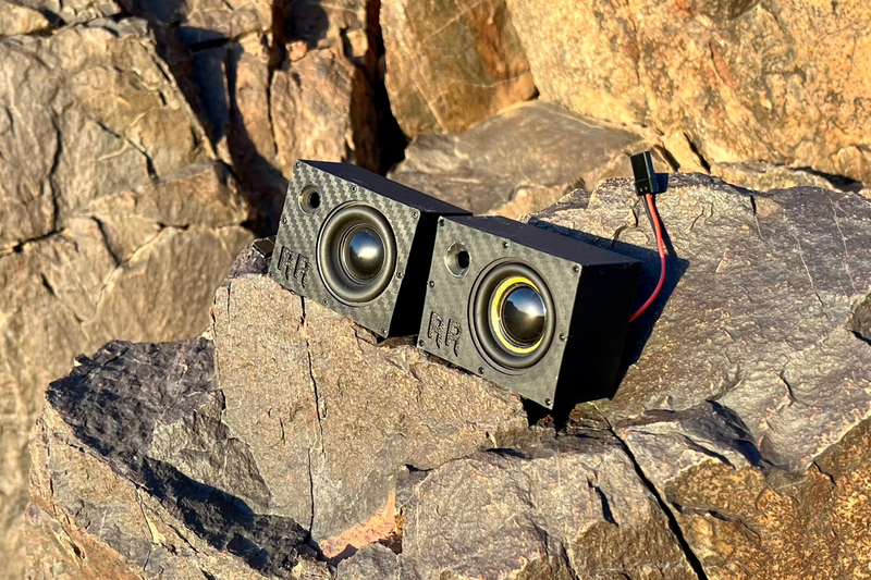 A pair of Super Single speakers lined up along a rock ledge with their leads trailing off to one side. 1/10 scale.