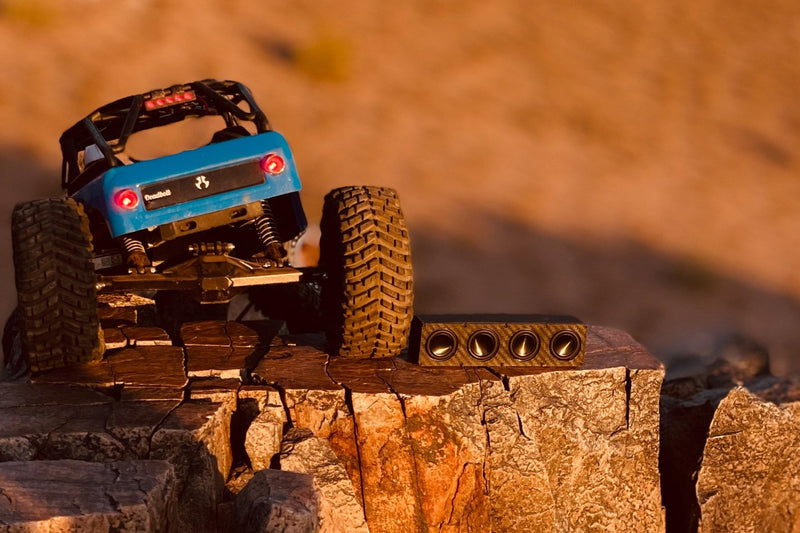 The Quad lying on orange rock at sunset with a blue RC crawler on the ledge above. 1/10 scale.