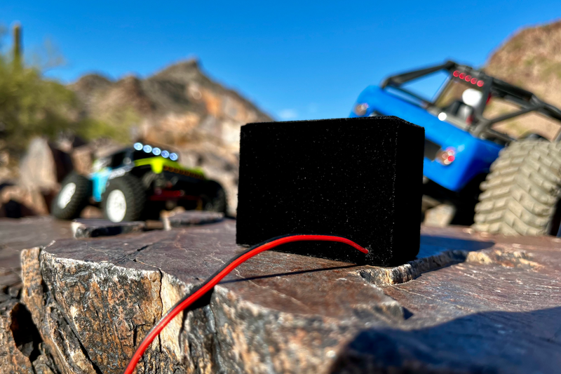 The Super Single in black suede wrap on rock with a blue RC crawler behind it. 1/10 scale RC speaker.