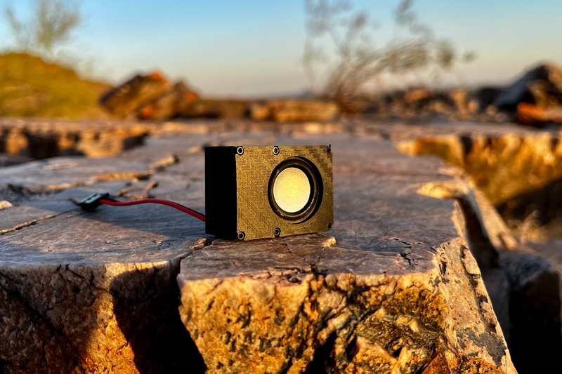 The Micro Single standing on cracked desert rock at sunset, gold carbon-look face and 23 mm driver, receiver lead trailing behind. 1/24 and 1/18 scale.