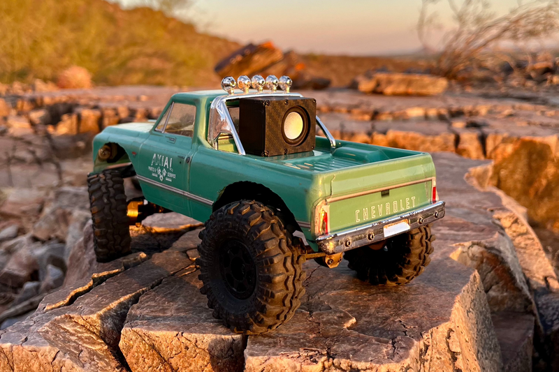 Rear view of a green Chevrolet-bodied RC pickup on rock with The Micro Single mounted behind the cab. 1/24 and 1/18 scale.