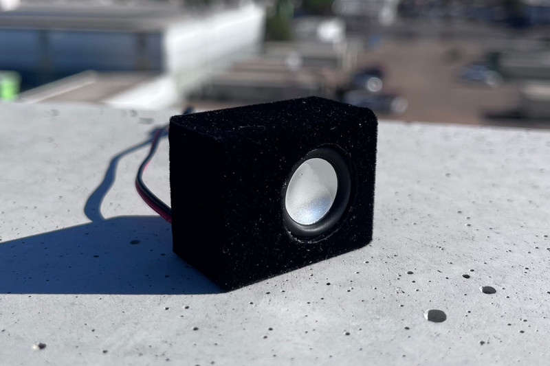The Micro Single in black suede wrap on a concrete ledge, single driver facing forward. 1/24 and 1/18 scale RC speaker.