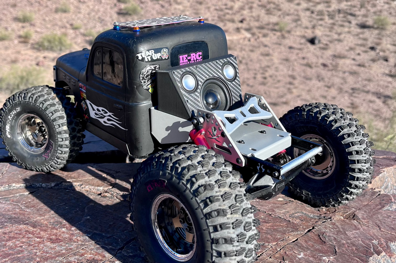 A black comp crawler on rock with The Overkill for Hardline Bed mounted across its front end. 1/10 scale.