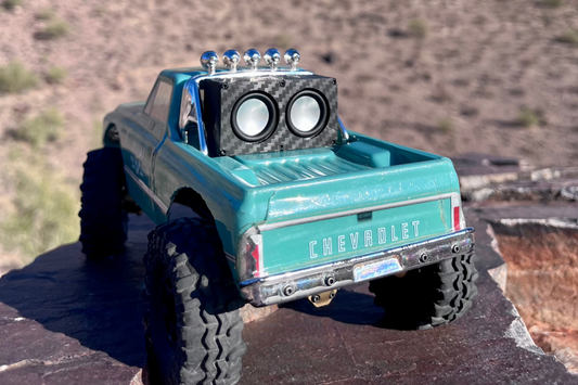 The Micro Double mounted above the windshield of a teal Chevrolet-bodied RC crawler on desert rock, front view. 1/24 and 1/18 scale.