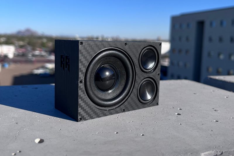 The Overkill on a concrete rooftop with the black-cone 52 mm driver and RR logo forward, office building behind. 1/10 scale.