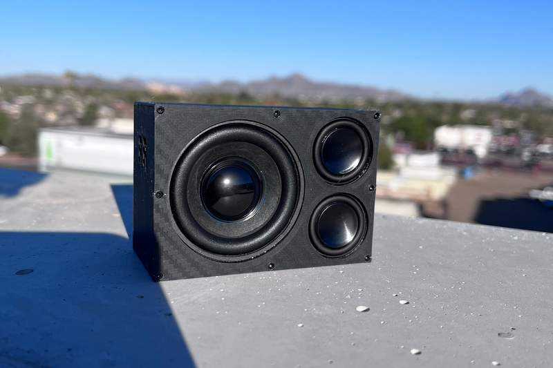 The Overkill with a black-cone 52 mm driver on a concrete rooftop, city skyline behind. 1/10 scale RC speaker.