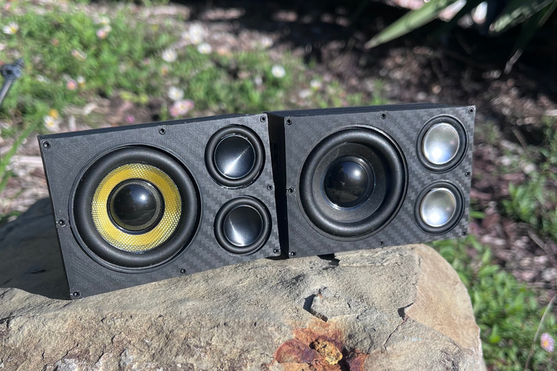 A pair of Overkill speakers standing together on a rock, yellow cone and black cone alongside each other. 1/10 scale.