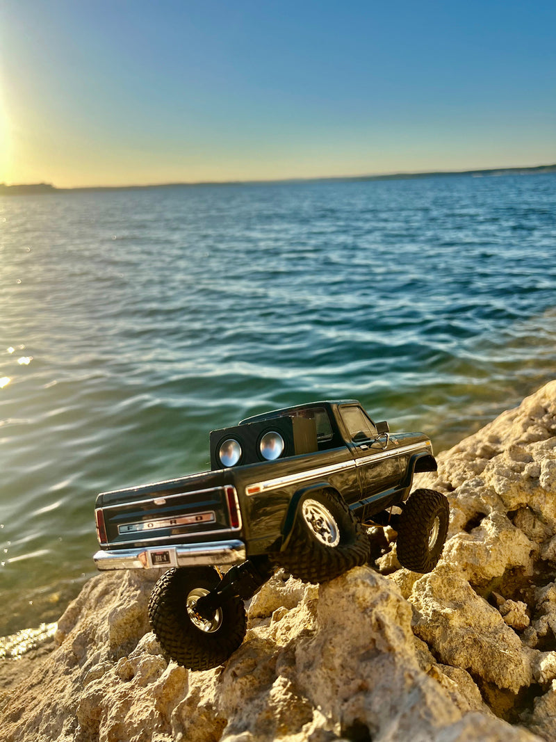 A black RC pickup carrying The Double on a rock ledge above a lake at sunset. 1/24, 1/18 and 1/10 scale.